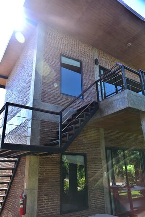 Un edificio de varios pisos con fachada de ladrillo, una escalera con barandillas de metal y ventanas grandes.