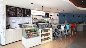 Interior moderno de una cafetería con un tablero de menú, una vitrina de vidrio con bebidas y una zona de bar con taburetes.