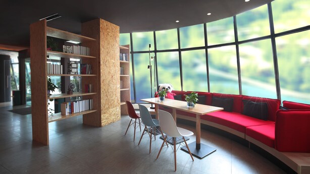 Un rincón de lectura moderno con un sofá rojo, estanterías de madera y una mesa con sillas.