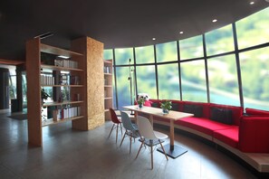 Een moderne leeshoek met een rode bank, houten boekenplanken en een tafel met stoelen.
