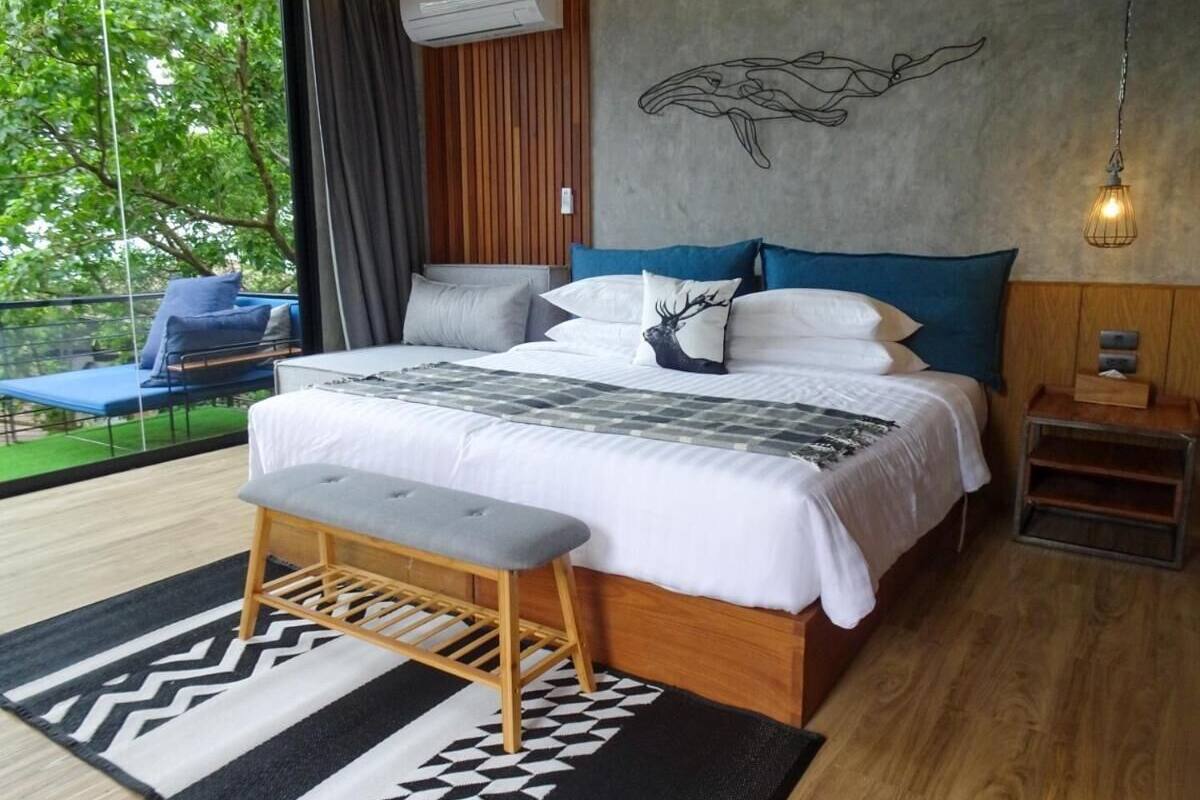 A bedroom with a large bed, a bench, a wall mural, and a view of the outdoors.