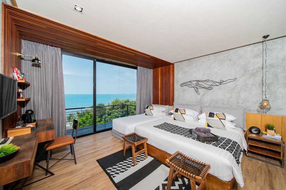 A modern hotel room with a large bed, a desk, and a view of the ocean.