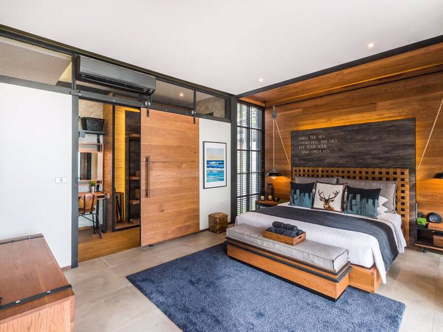 A modern bedroom with a large bed, wooden accents, a mounted TV, and a view of the sea.