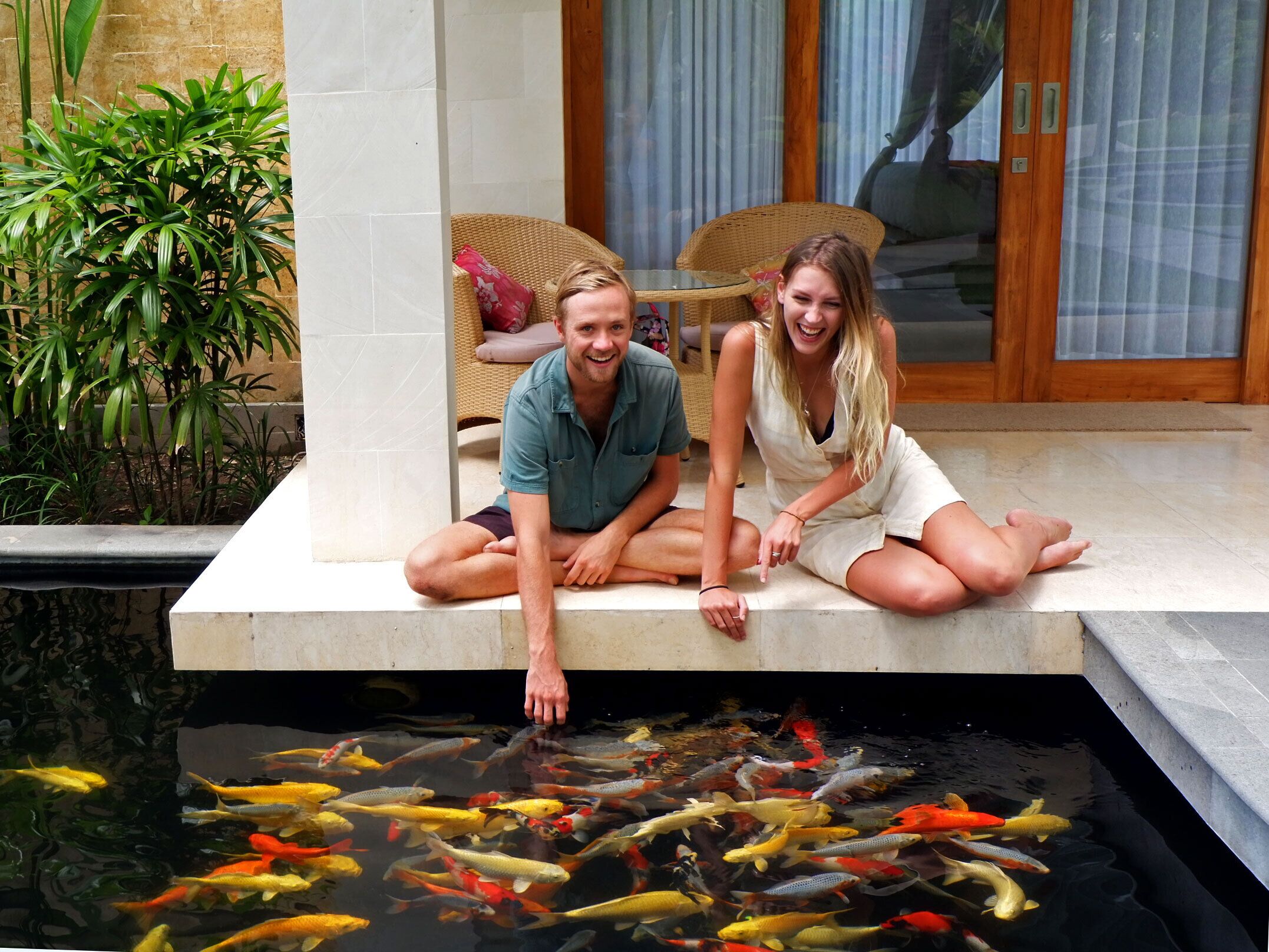 A couple sitting on a stone ledge overlooking a koi pond.