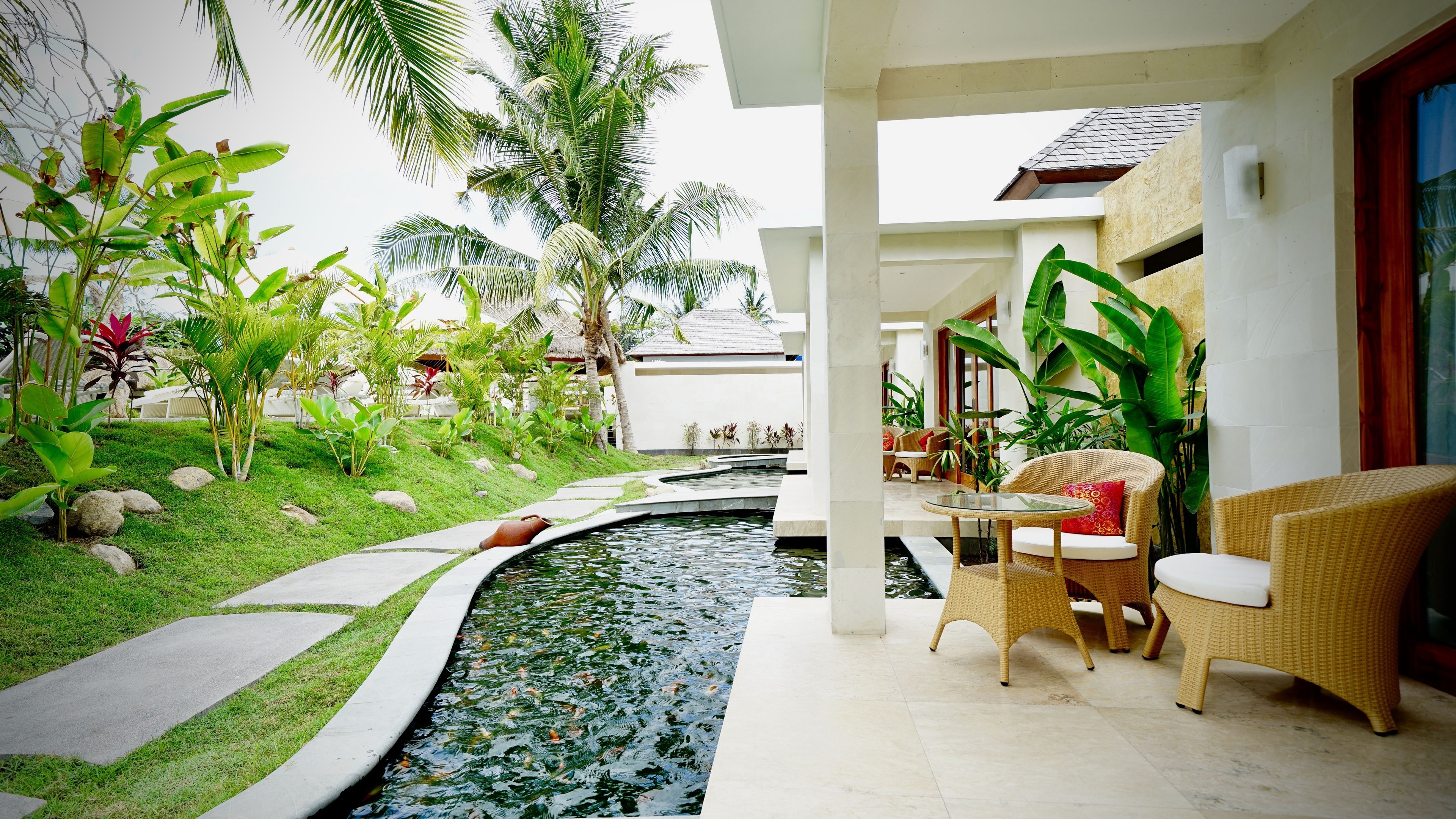 Un jardín interior tranquilo con fuente, zona de estar y plantas tropicales.