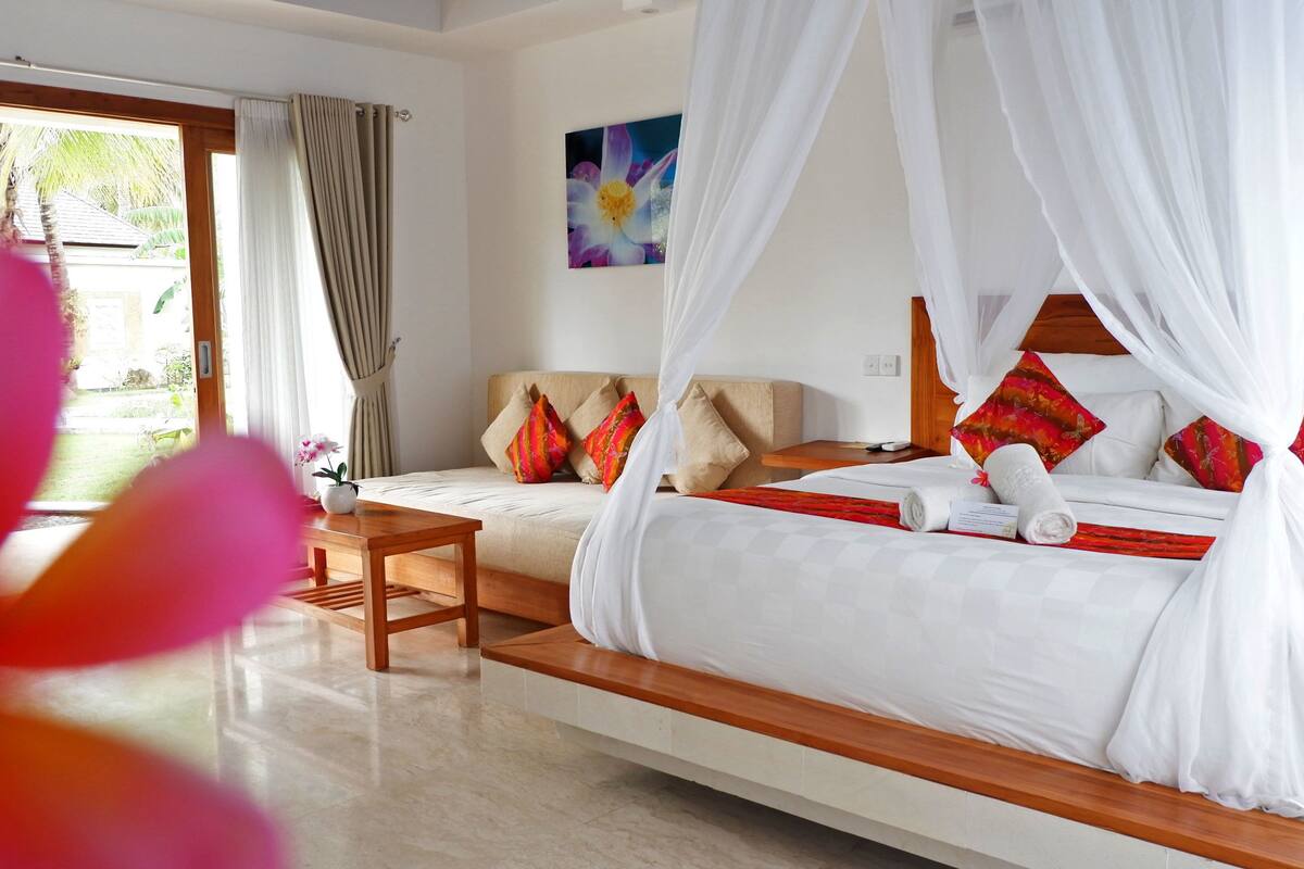 A bedroom with a four-poster canopy bed, a wooden bedside table, and a small desk.