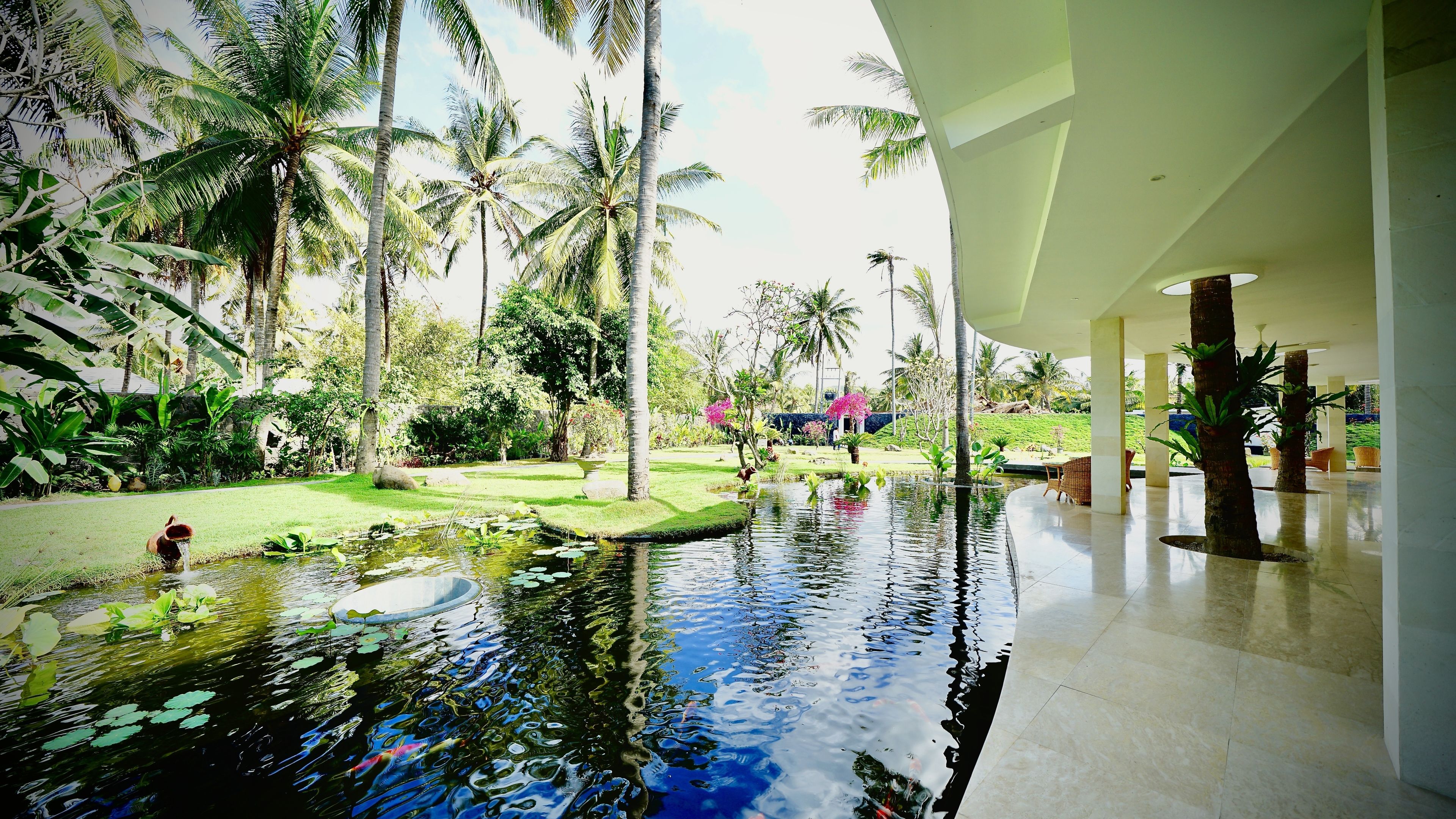 A serene indoor garden with a central water feature, surrounded by lush greenery and palm trees.