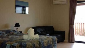 Quarto de hotel com cama, sofá de couro preto, pintura na parede e aparelho de ar condicionado.