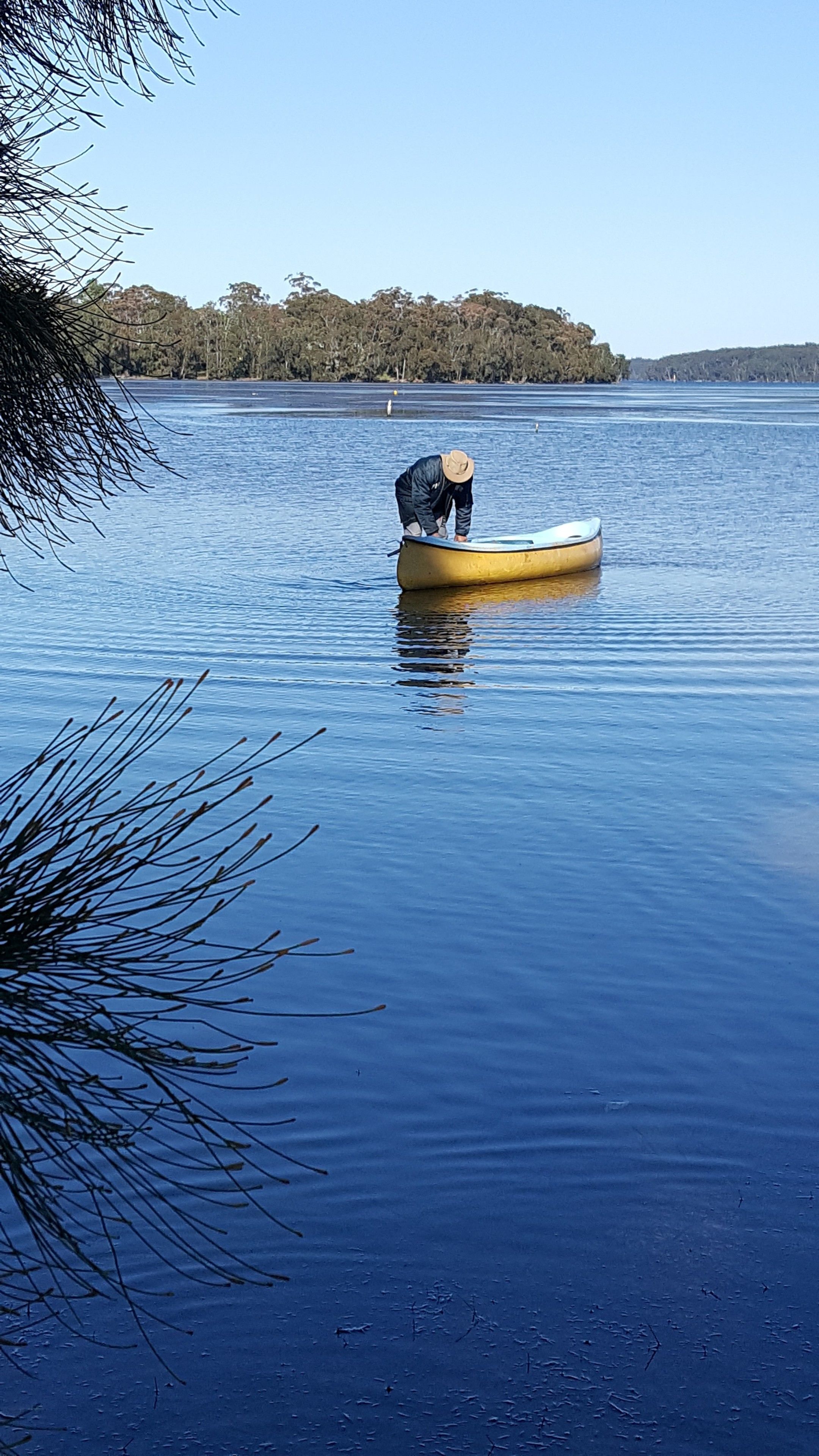 Une personne est dans un canoë jaune sur un lac paisible, avec des arbres en arrière-plan.
