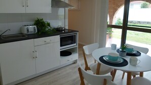 A modern kitchen with white cabinets, a black countertop, a toaster, a microwave, and a dining area with a white table and chairs. - The Sanctuary at Paradise Beach (Sanctuary Point)