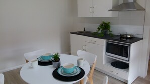 A modern kitchen with white cabinets, a microwave, and a sink. There is a dining table with chairs and a small potted plant. - The Sanctuary at Paradise Beach (Sanctuary Point)