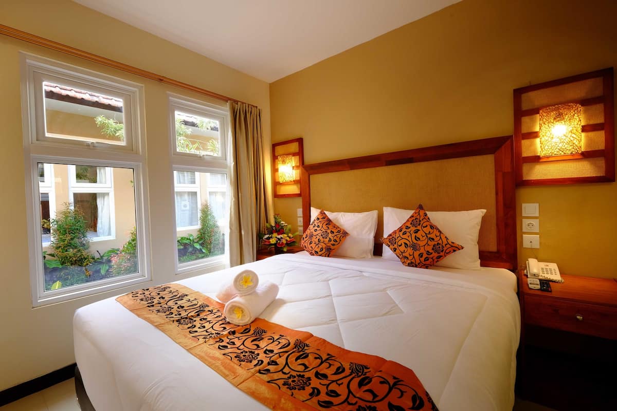 A hotel room with a large bed, two bedside tables, a nightstand, and a window with curtains.