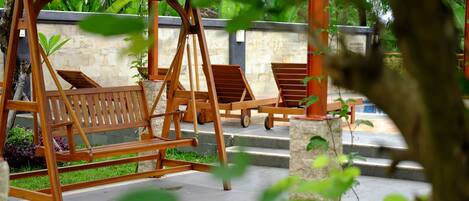 A wooden swing set with two chairs, a stone wall, and a red umbrella in the background.