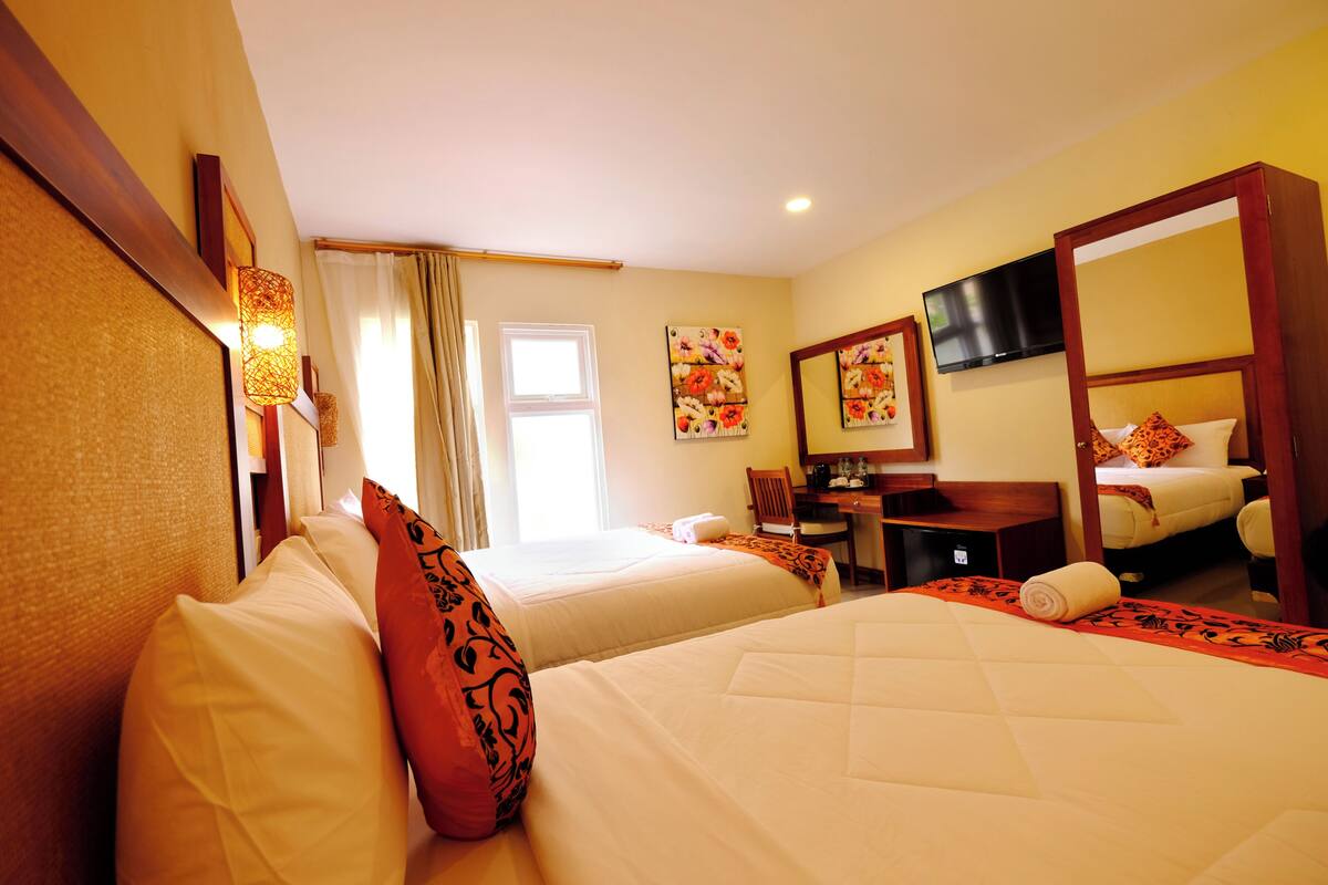 A hotel room with two beds, a desk, a chair, a television, and a window with curtains.