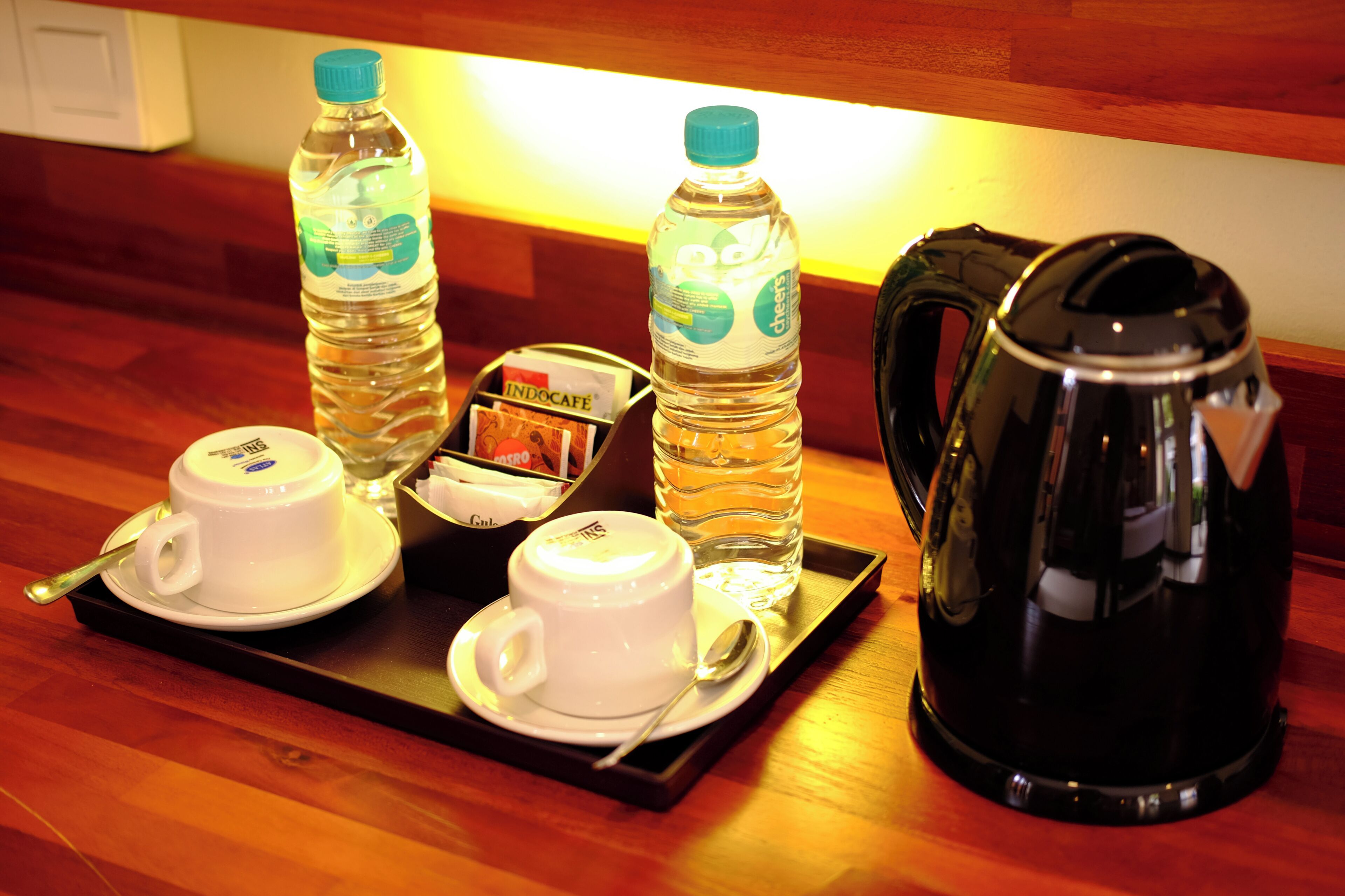 Un plateau avec deux tasses, deux bouteilles d’eau, une petite horloge et une cafetière, posés sur une table en bois.