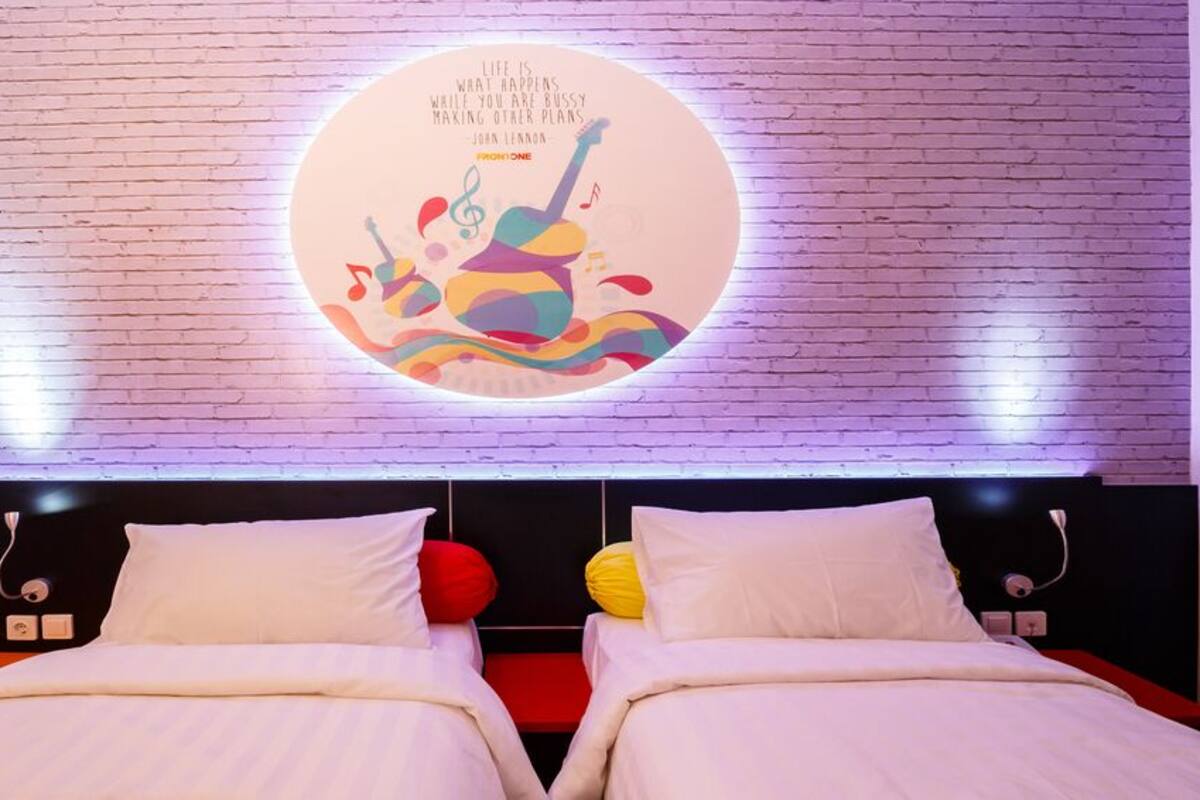 A hotel room with a brick-patterned wall, a circular light fixture with a quote, and two beds with white bedding and colorful pillows.