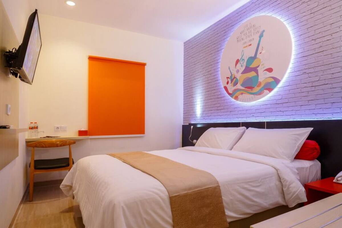 A modern hotel room with a bed, a desk, a chair, and a wall-mounted TV.
