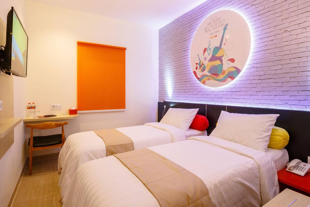 A hotel room with two beds, a desk, a chair, a TV, a wall clock, a phone, and a wall with a circular design.