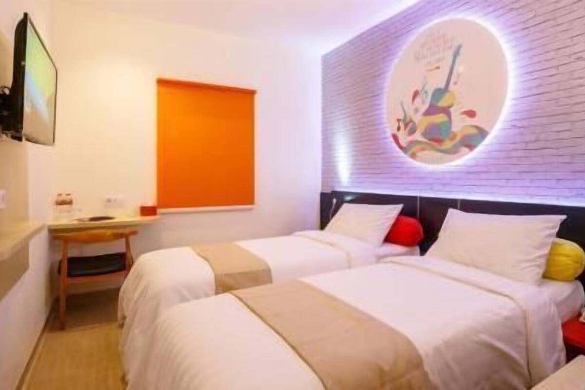 A hotel room with two beds, a desk, a red nightstand, and a wall-mounted phone.