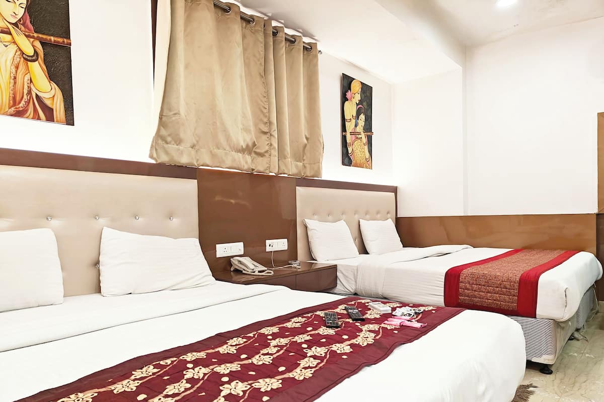 A hotel room with two beds, a telephone on the nightstand, and a decorative red and gold bedspread.