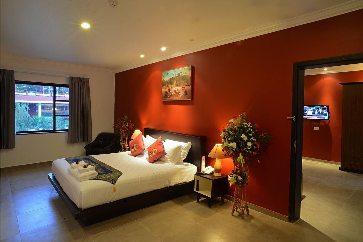 Ein Hotelzimmer mit einem großen Bett, einem Nachttisch mit Lampe, einem Bild an der Wand und einem Fernseher in der Ecke.