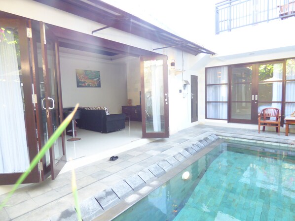 A residential setting with a swimming pool, a sofa, and a dining area. - Angel Villas Kesari (Denpasar)
