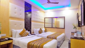 A hotel room with two beds, a ceiling fan, a mirror, a TV, and a small desk with a vase of flowers. - Check In Room New Delhi Railway Station (New Delhi)