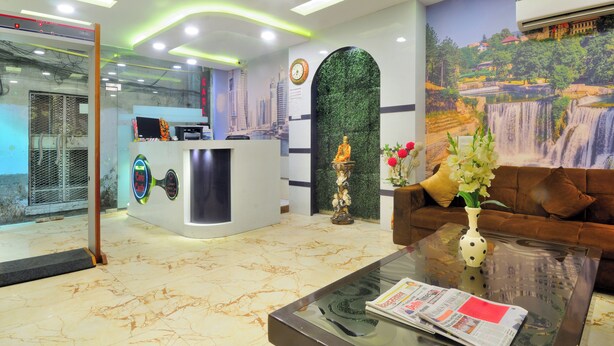 A hotel reception area with a reception desk, a sofa, a coffee table with a vase and newspaper, and a mural of a waterfall. - Check In Room New Delhi Railway Station (New Delhi)
