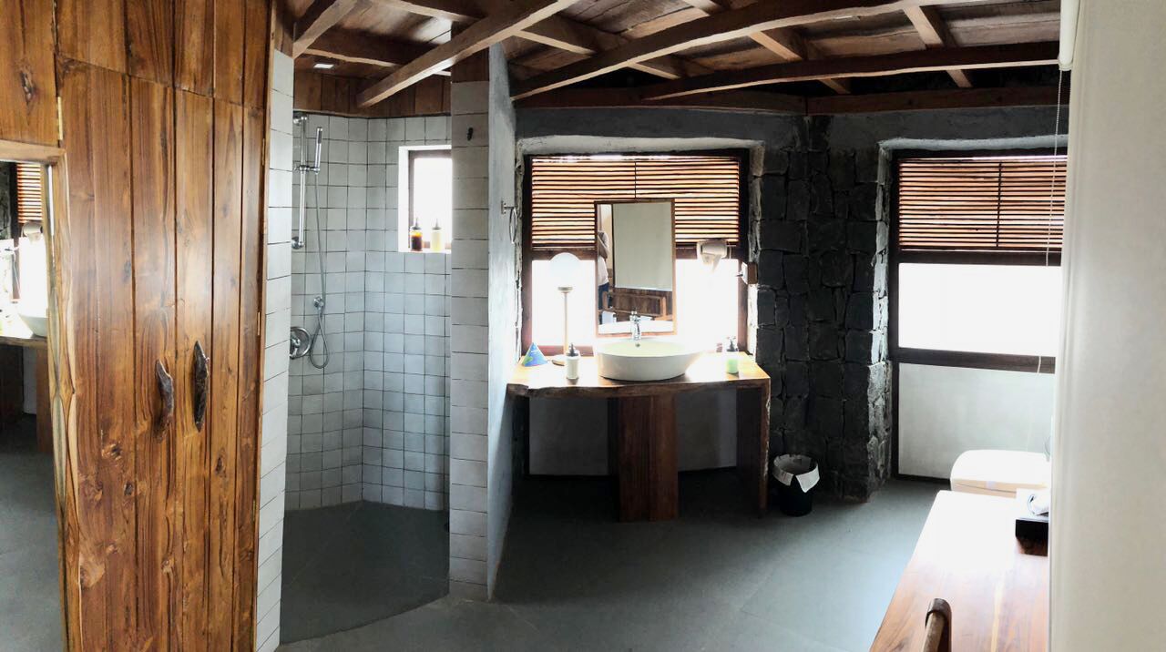 Un baño rústico con puerta de madera, ducha, lavabo con espejo y ventana con persianas.