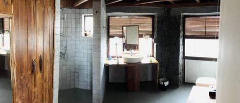 Un baño rústico con puerta de madera, ducha, lavabo con espejo y ventana con persianas.