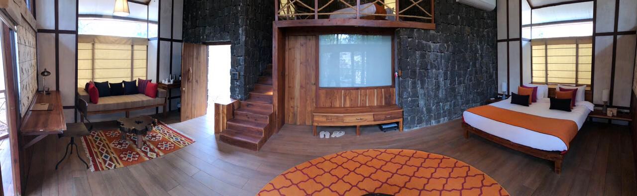A spacious bedroom with a large bed, a wooden bench, and a stone wall.