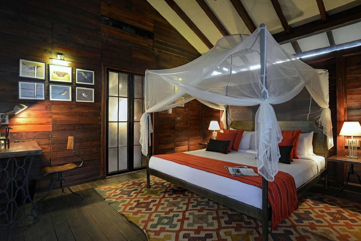 A wooden room with a bed under a canopy, a desk with a chair, and framed pictures on the wall.