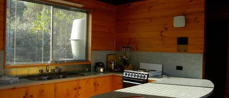 A compact kitchen with wooden cabinets, a gas stove, a sink, and a window with blinds.