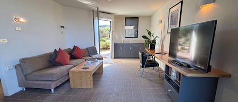 A modern living room with a sofa, coffee table, TV, and kitchen area.
