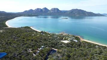 Vista aérea de una zona costera con playa, aguas azules cristalinas y montañas al fondo.