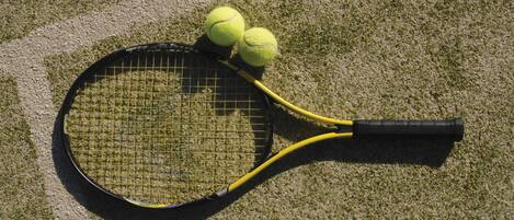 A tennis racket with two tennis balls on a grass court.
