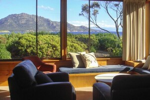Una habitación con un ventanal que ofrece vistas a un paisaje montañoso y una masa de agua. Hay dos sofás y una mesita.