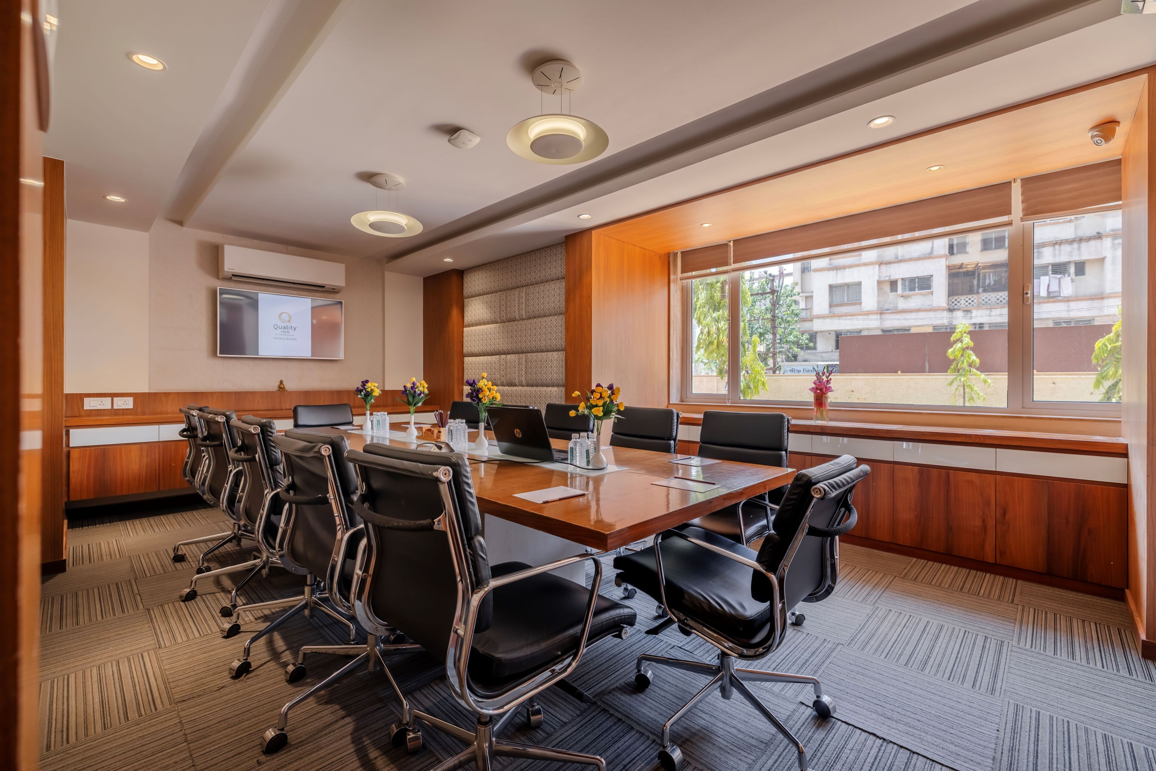 A conference room with a long table, black chairs, and a large window with a view of buildings and trees.