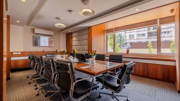 A conference room with a long table, black chairs, and a large window with a view of buildings and trees.