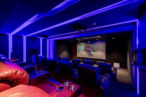 Cinema com poltronas reclináveis de couro vermelho e uma tela grande.