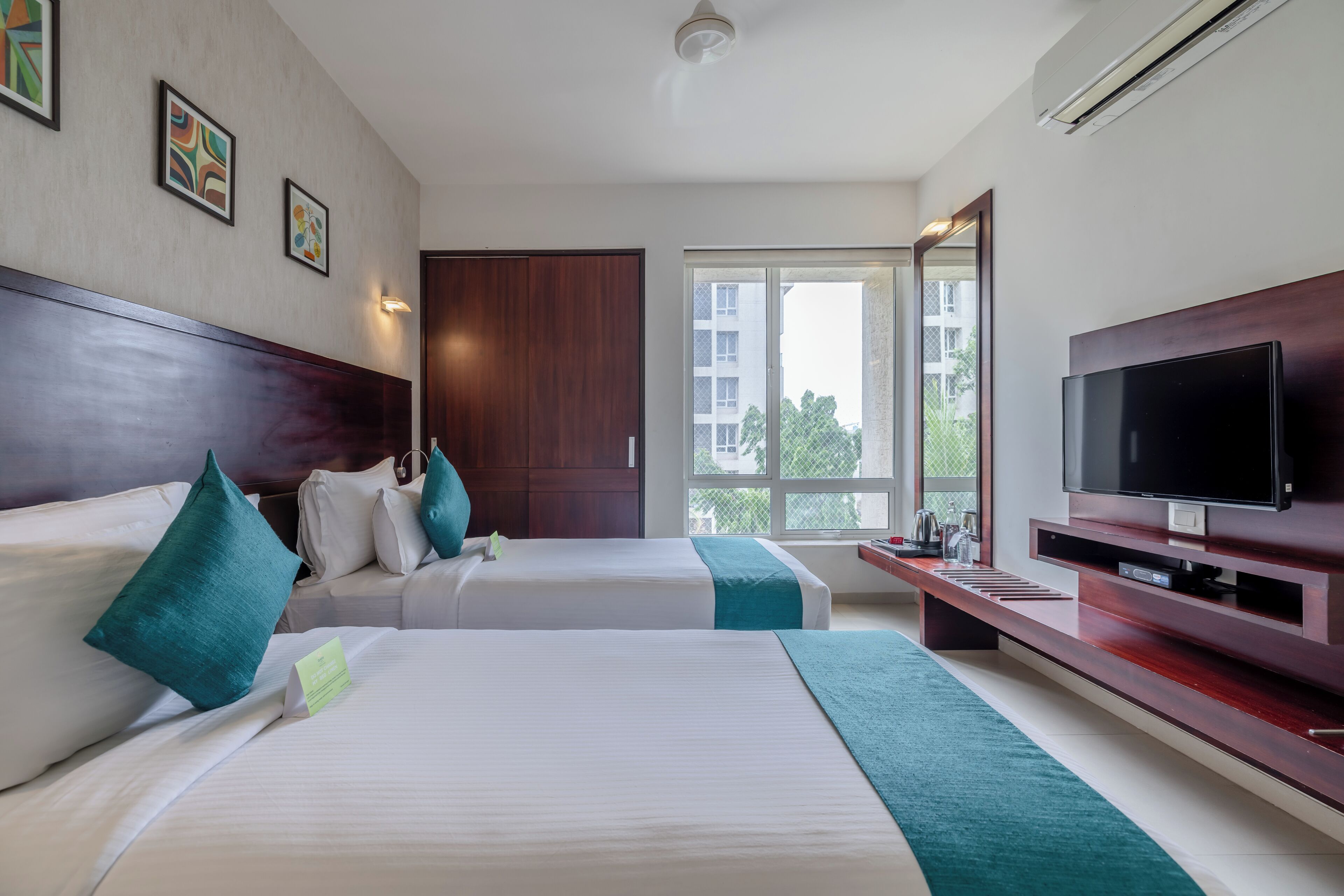 Habitación de hotel con dos camas, un televisor y un ventanal grande.
