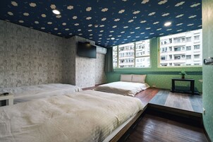 Una habitación con dos camas, televisión y ventana con vista a un edificio.