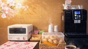 A kitchen area with a toaster, a coffee machine, a basket of pastries, and a cup of coffee. - Sofu Hotel (New Taipei City)