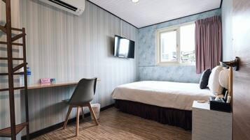 Ein Schlafzimmer mit Bett, einem an der Wand montierten Fernseher, einem Fenster mit Vorhängen, Holzboden und einem Schreibtisch mit Stuhl.