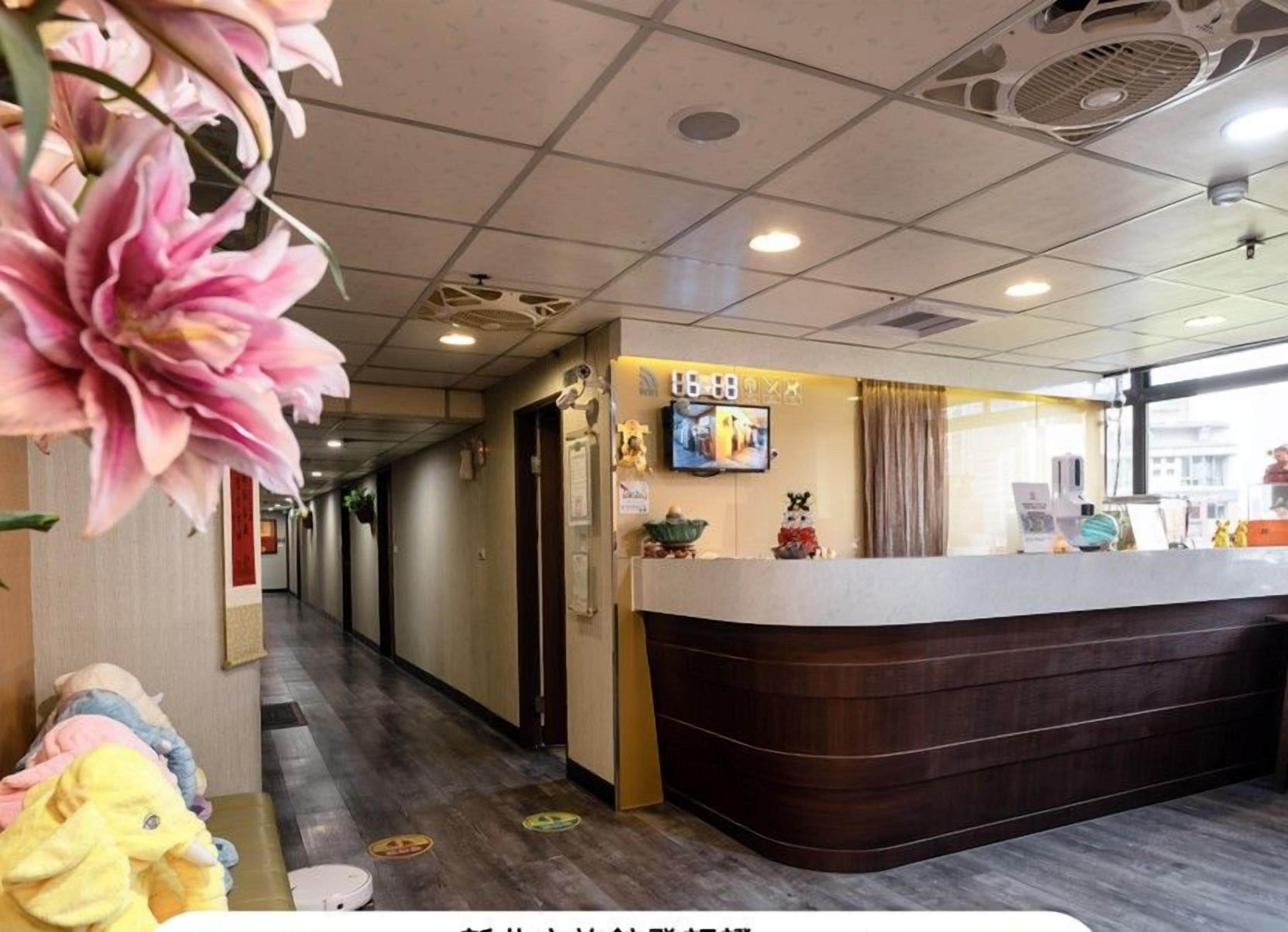 Et hotellets receptionsområde med en træreception, et fjernsyn og et vindue med gardiner.