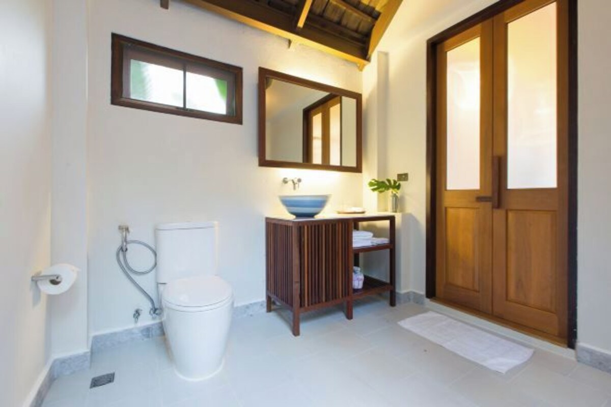 Een badkamer met toilet, wastafel, spiegel en houten deur.