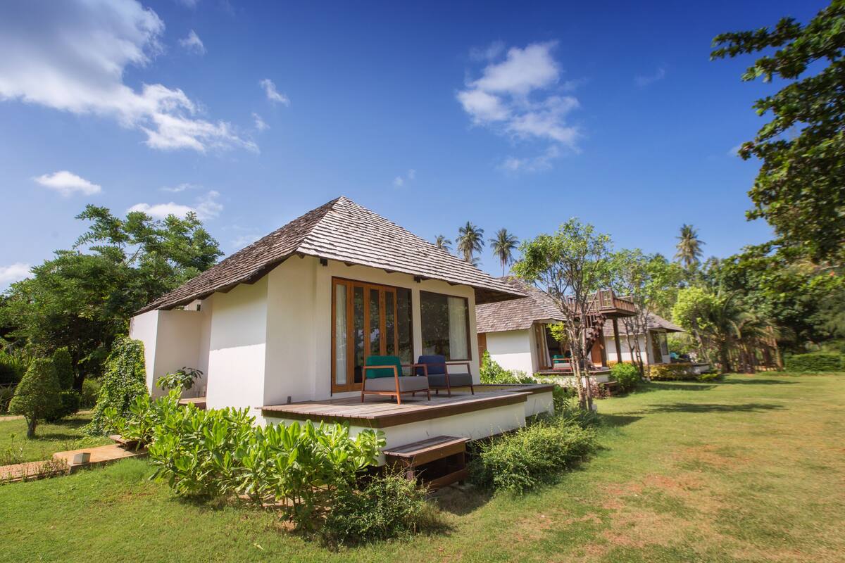 A bungalow with a tiled roof, large windows, and a porch with seating.
