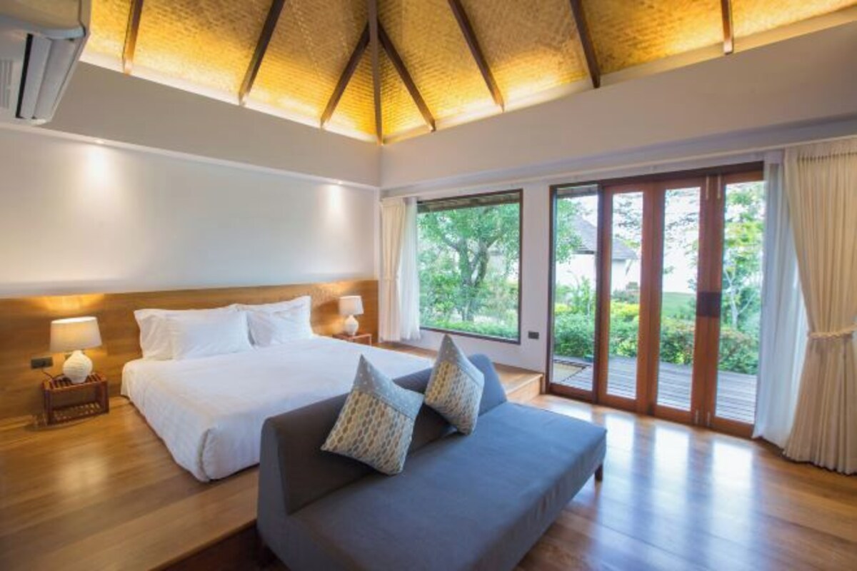 Een ruime slaapkamer met een groot bed, een bank en uitzicht op de omgeving via een schuifdeur.