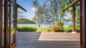 Une terrasse en bois mène à un point de vue donnant sur une plage bordée de palmiers et où l’on aperçoit une montagne au loin.