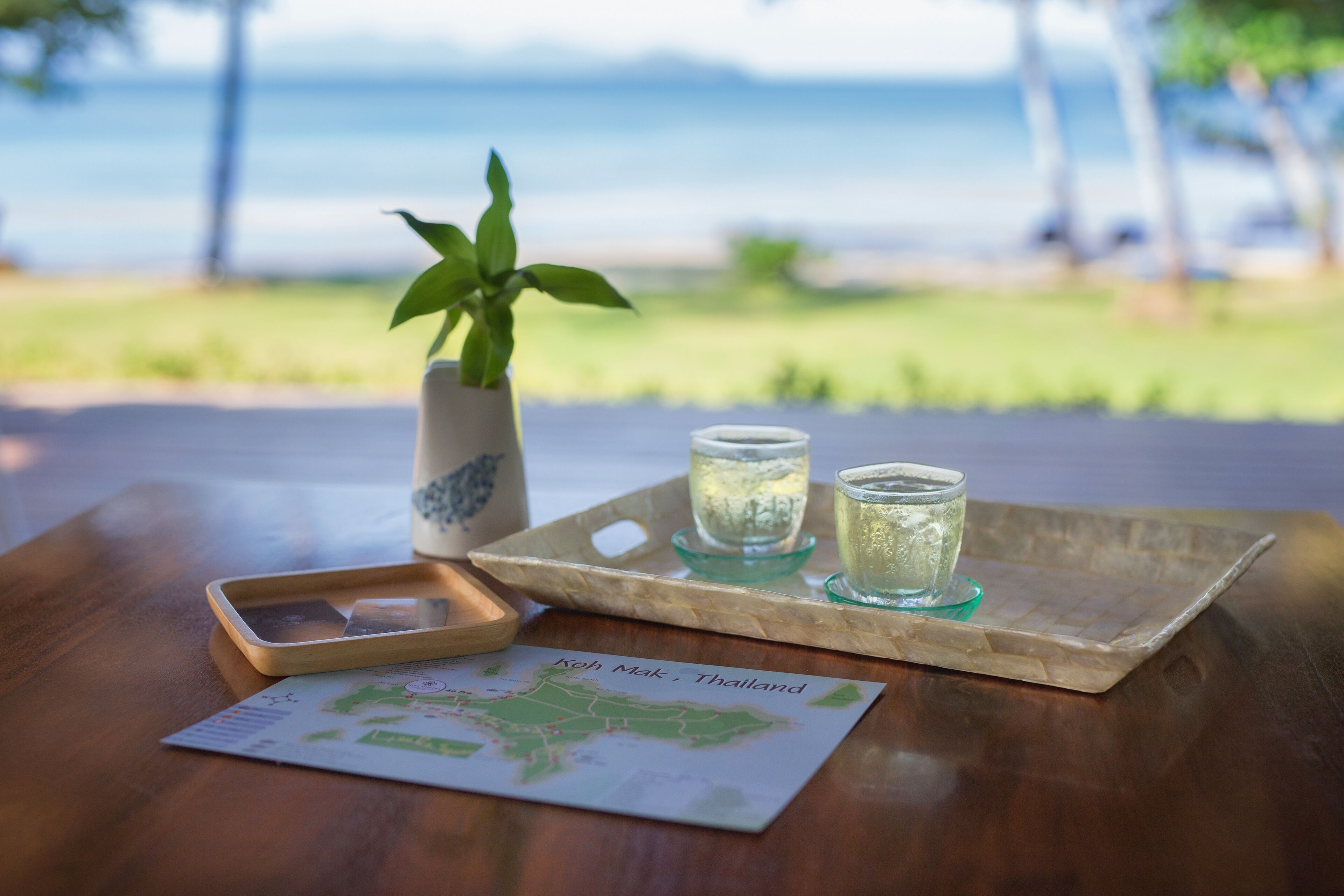 A wooden table with a tray holding two glasses of water, a map of Thailand, and a potted plant.